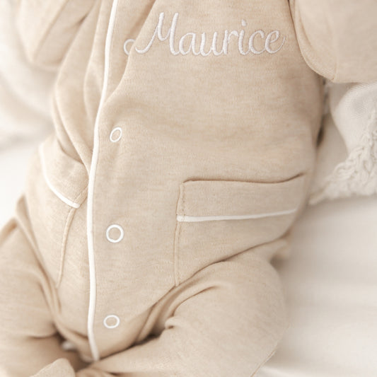 Detail van Kruippakje Lou – witte bies en fijn geborduurde naam, luxueuze afwerking voor babykleding