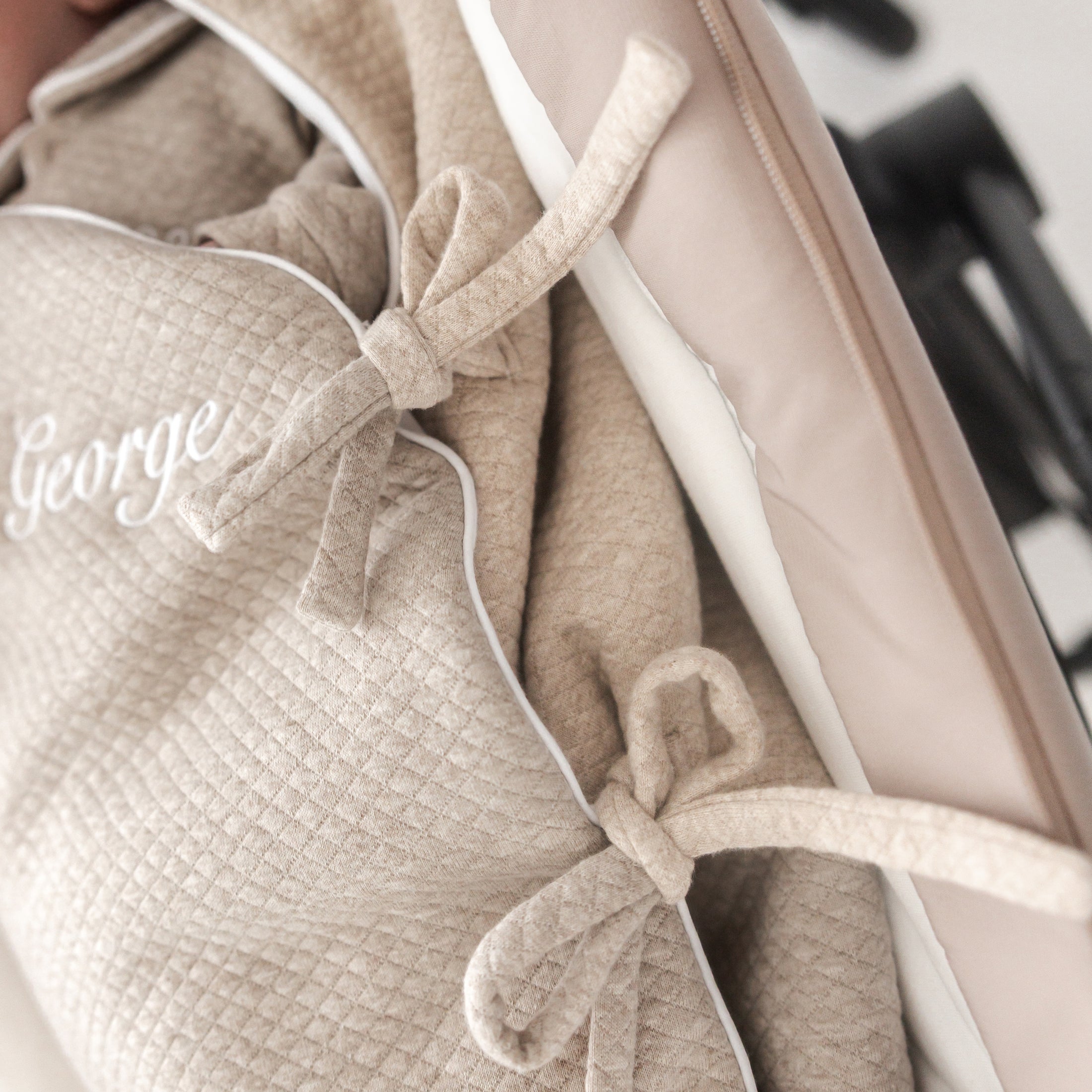 Detail van beige voetenzak voor kinderwagen – strikjes aan de zijkant en fijne bies voor elegante afwerking